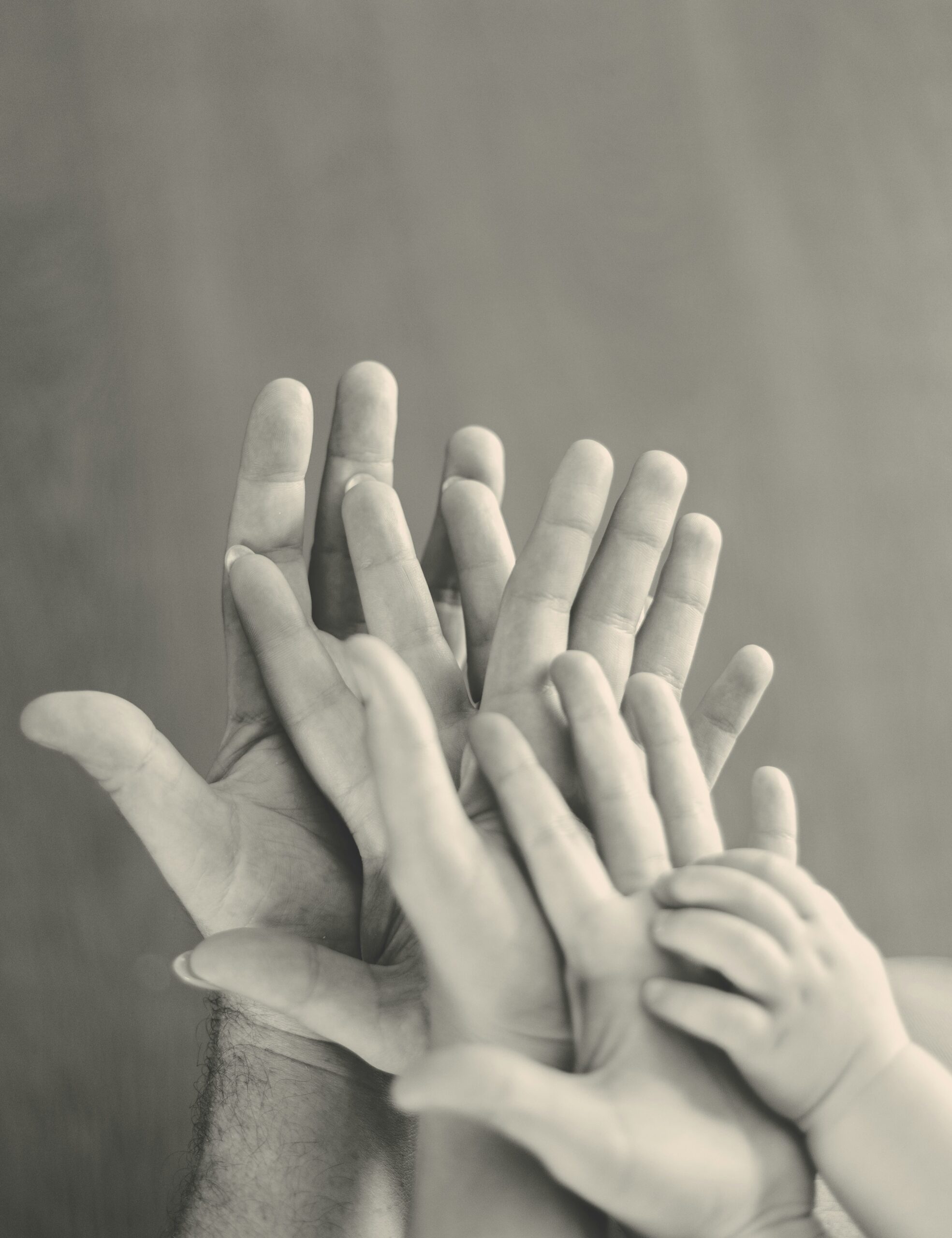 A black and white photo showing overlapping hands of different sizes, from adult to child, symbolizing family, support, and connection.